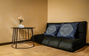 A room with a black sofa, a round table with a vase of flowers, and two decorative pillows with circular patterns. - meisei ebiya (Osaka)