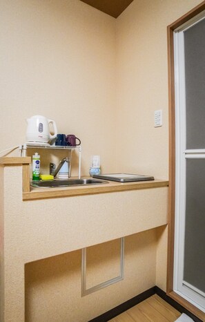 A compact kitchenette with a built-in sink, a coffee maker, and a small shelf with mugs and cleaning supplies. - meisei ebiya (Osaka)