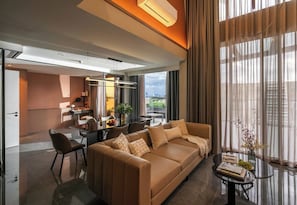 A modern living room with a sofa, a dining table, and a view of the city through large windows. - Luxury Residence at Metropole (Ho Chi Minh City)