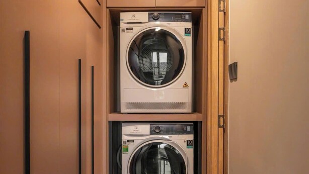 Une buanderie équipée de deux machines à laver à chargement frontal superposées, d’une porte en bois et d’un sol carrelé.