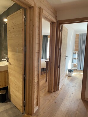 A modern interior with wooden paneling, a visible bathroom with a sink, and a hallway leading to a bedroom with a bed and curtains. - Les Planches de Villard 5* Chalet – Terrace, sauna – Alpe d’Huez area (Villard-Reculas)