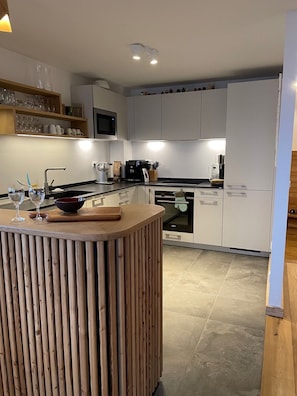 A modern kitchen with white cabinets, a wooden island, and a built-in oven. - Les Planches de Villard 5* Chalet – Terrace, sauna – Alpe d’Huez area (Villard-Reculas)