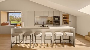 Een moderne keuken met een centraal kookeiland, barstoelen en uitzicht op groen.