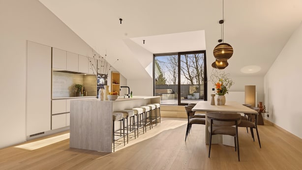 Een moderne keuken met een centraal eiland, barkrukken en een eethoek met een tafel en stoelen.