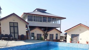 A swimming pool with a tiled edge, surrounded by a patio area with chairs and a small table. - The Rana Resort (Jogindarnagar)
