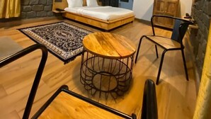 A cozy bedroom with a bed, a desk, and a chair. There is a ceiling fan, a rug, and a wall with a decorative piece. - The Rana Resort (Jogindarnagar)