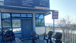 A resort's outdoor seating area with a signboard listing facilities like a 20x30 ft swimming pool, indoor & outdoor games, and a garden/lawn area. - The Rana Resort (Jogindarnagar)