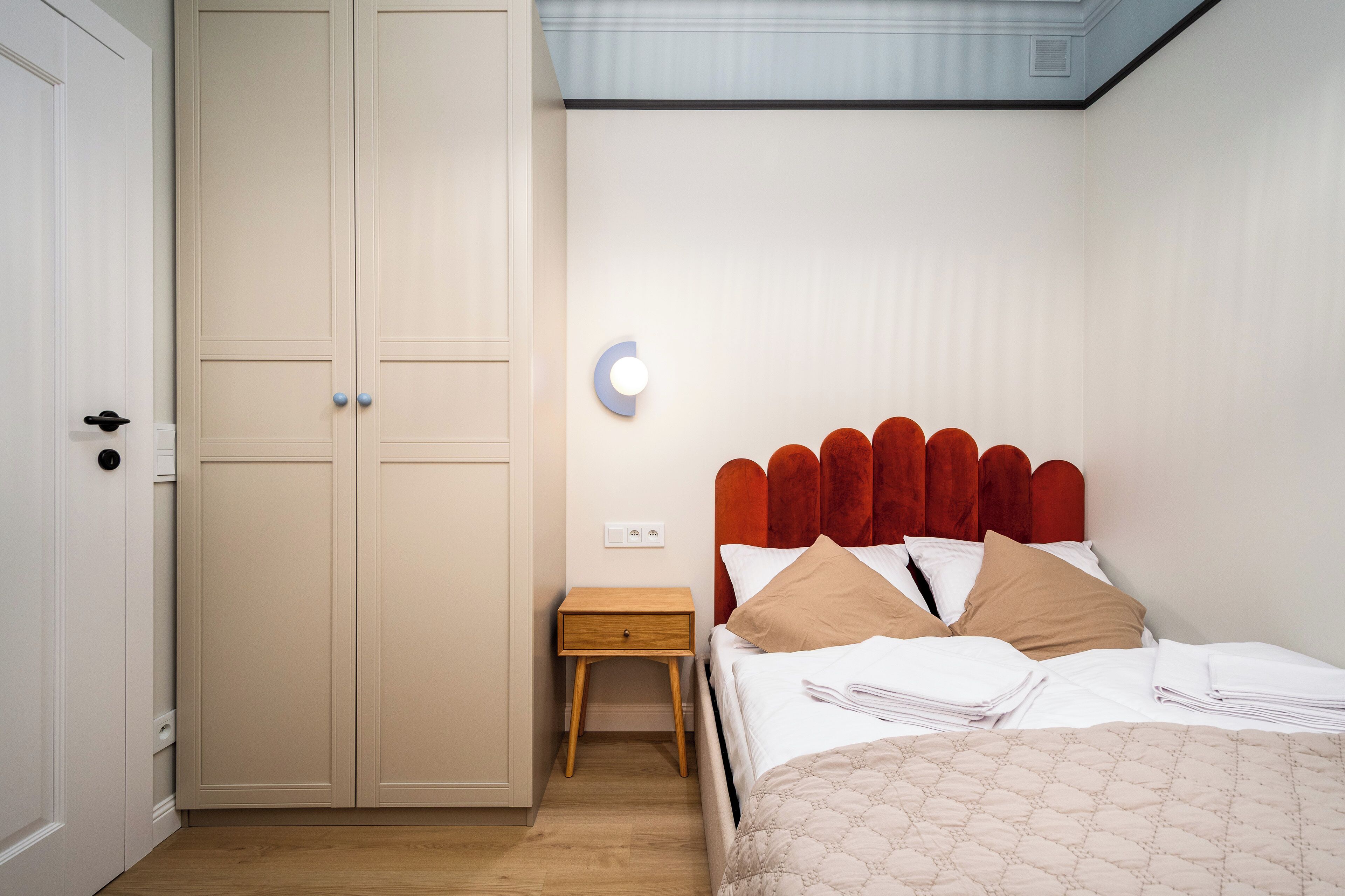 A bedroom with a bed, a nightstand, a wardrobe, and a wall-mounted light fixture.