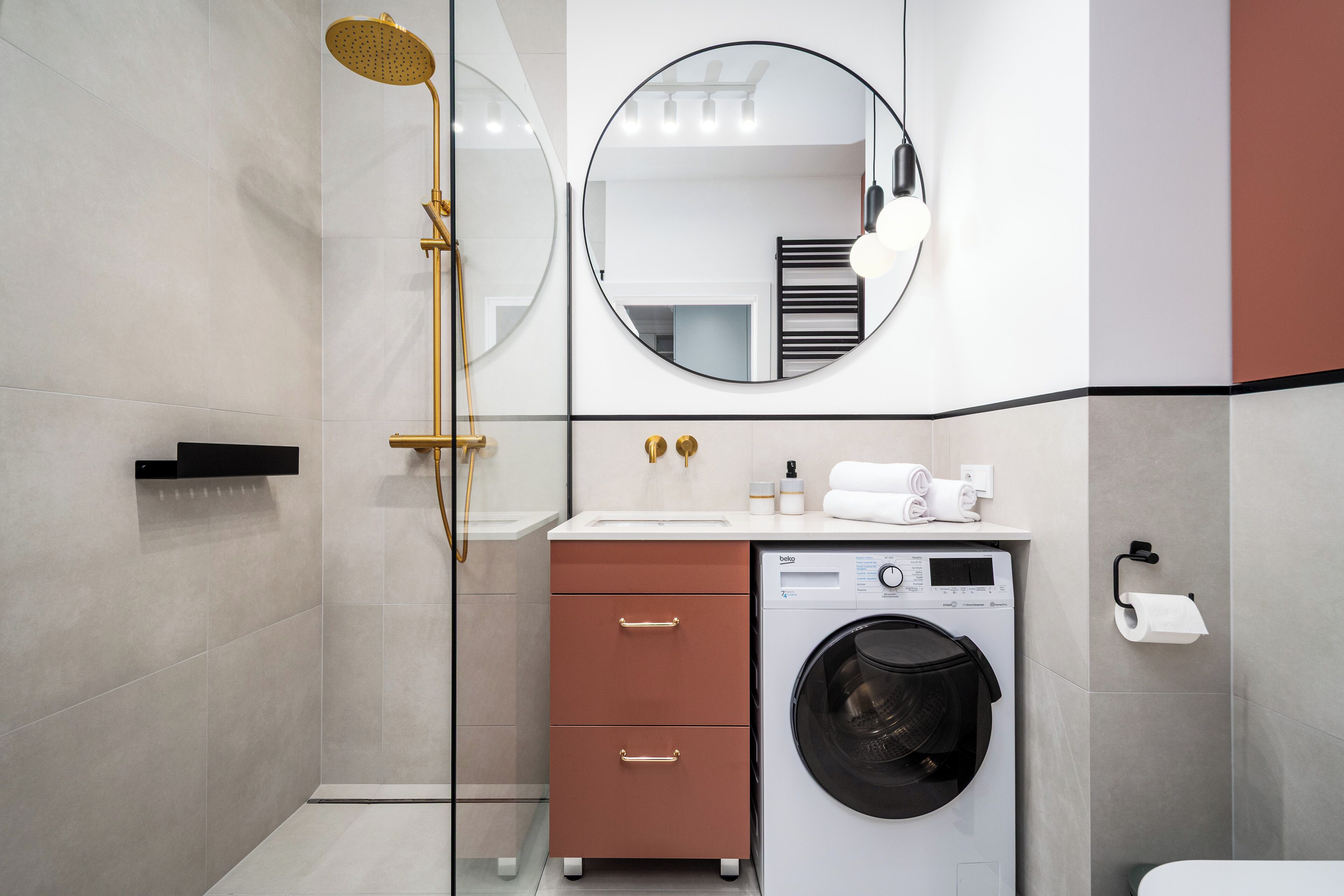 Een moderne badkamer met een glazen douchecabine, een ingebouwde wasmachine en een spiegel boven de wastafel.