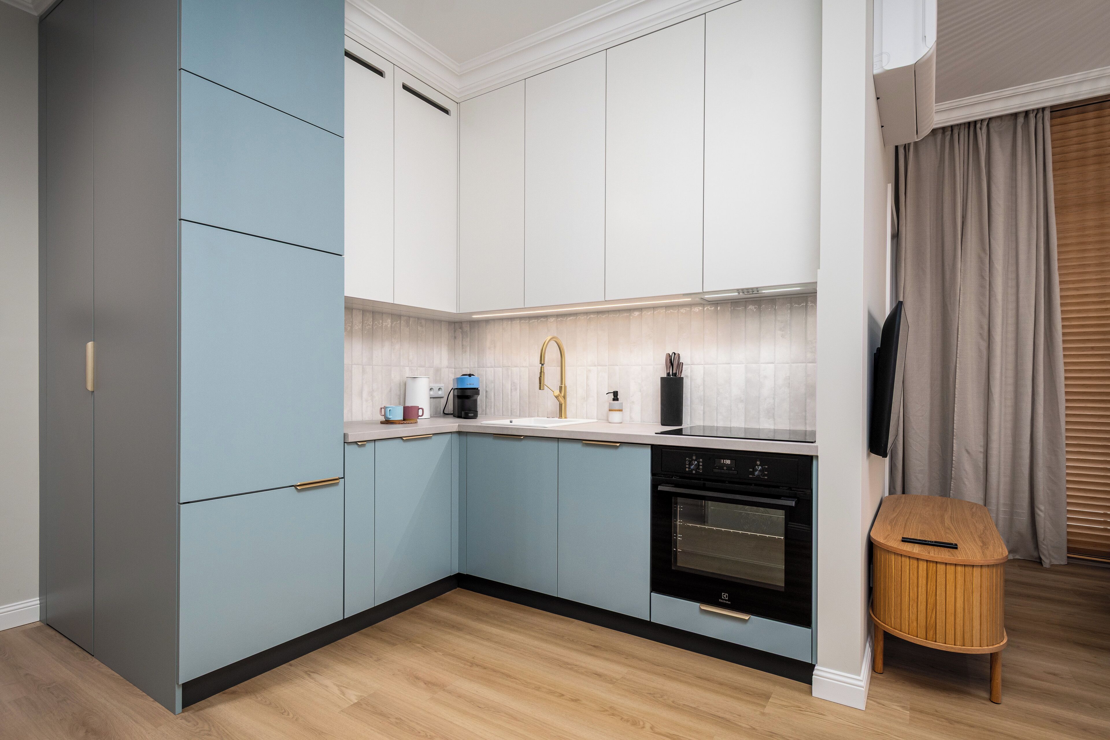 Eine moderne Küche mit hellblauen Schränken, einem schwarzen Backofen und einem Holztisch.
