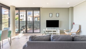 A modern living room with a grey sofa, a flat-screen TV, and a glass coffee table. - Mymogrohome – Modern Apartment with Sea View Terrace in Mogro (Mogro)