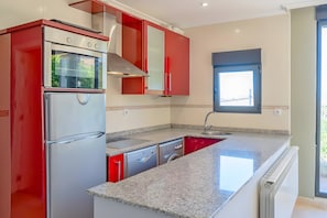 Una cocina con armarios rojos, electrodomésticos de acero inoxidable, encimera de granito y ventana con vistas.