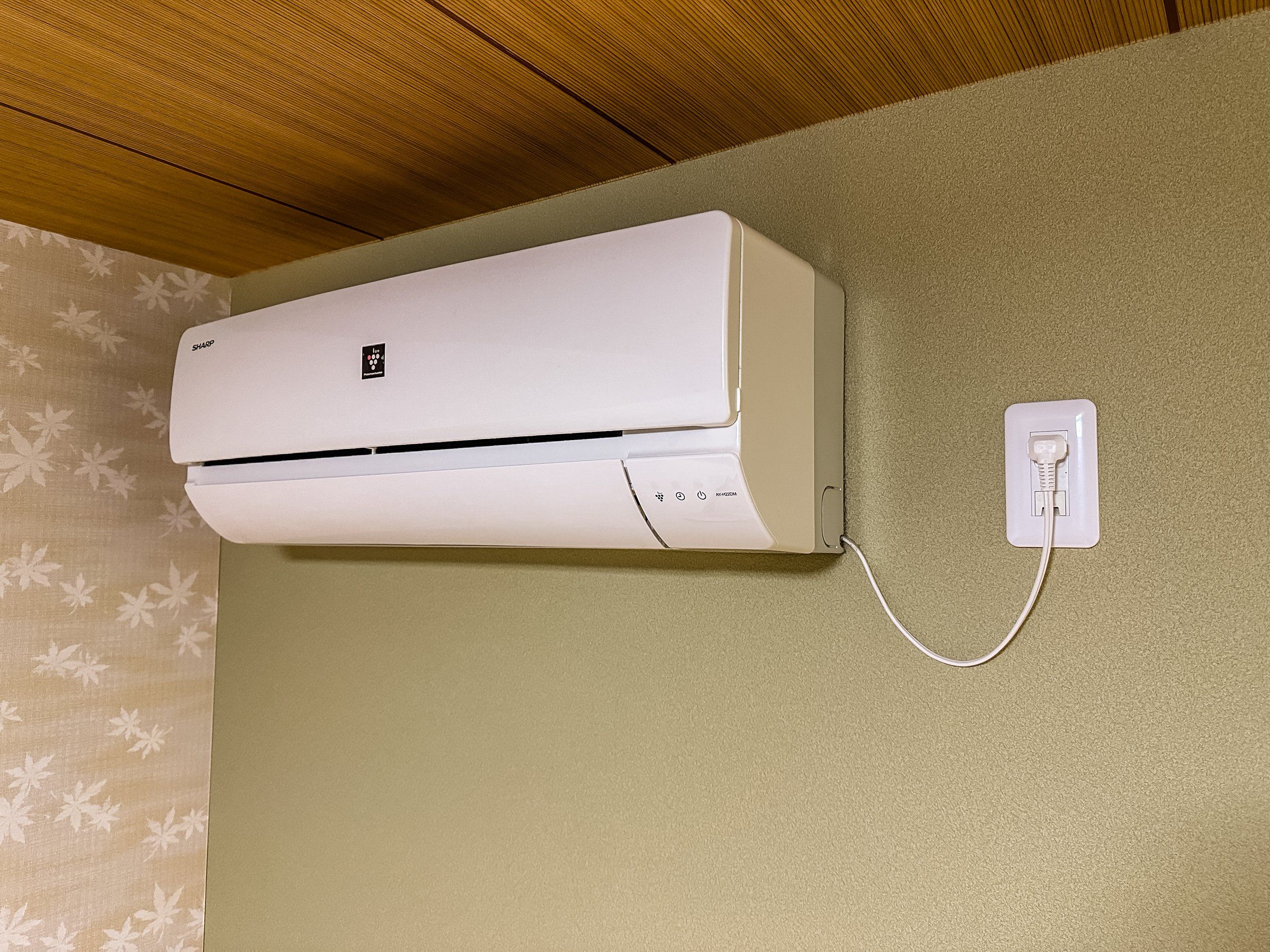 A wall-mounted air conditioner with a power cord plugged into a wall socket.