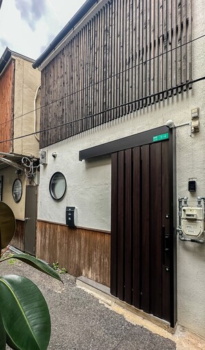 A building with a large wooden door, a small round window, and a security camera. - meisei ebiyaminami (Osaka)