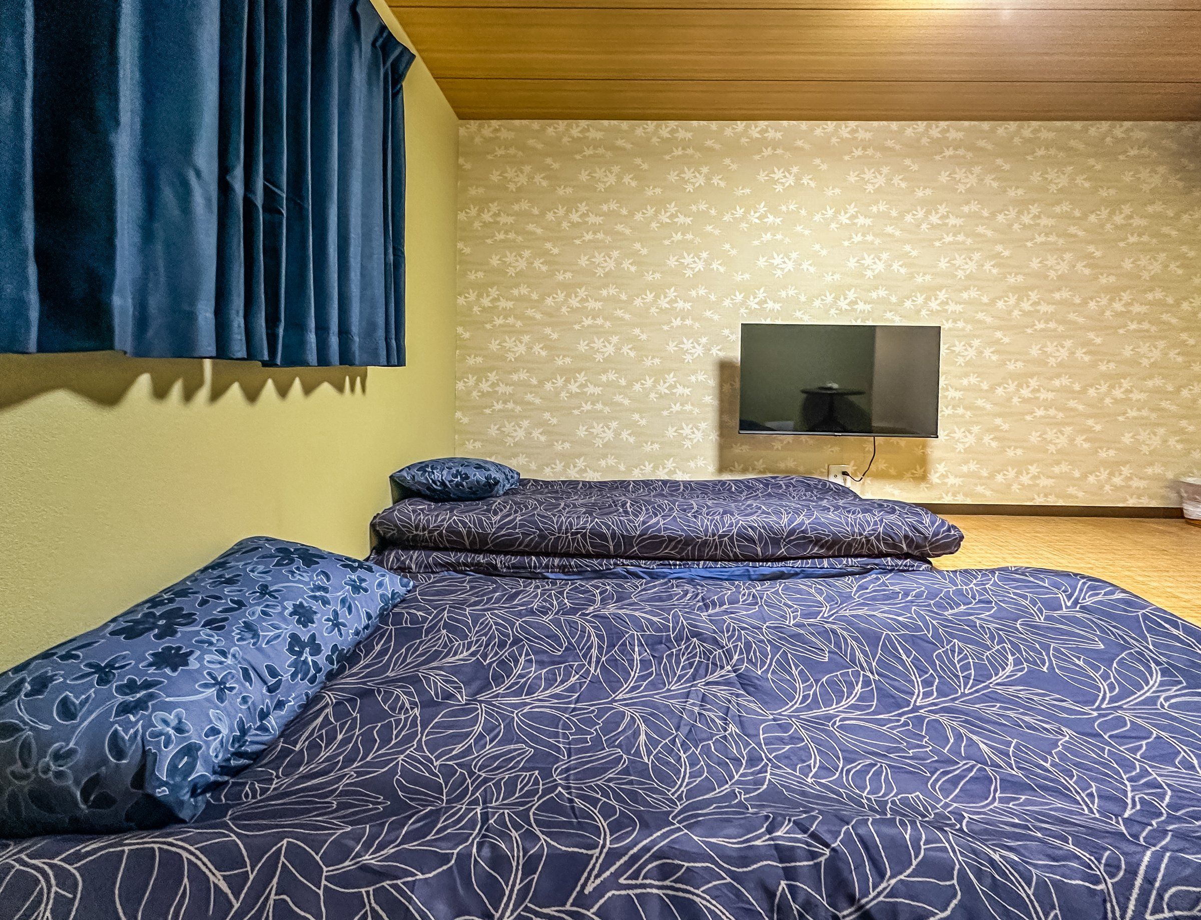 A bedroom with a bed, pillows, a television, and a patterned wall.