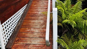 A wooden deck leading to a house with a white fence and lush green ferns. - Cosy retro renovated cottage with mountain setting out back (Queenstown)