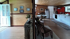 An open-plan living and dining area with a high ceiling, wooden walls, and a kitchen area. - Cosy retro renovated cottage with mountain setting out back (Queenstown)