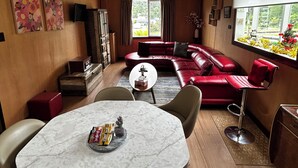 A modern living room with a red leather sofa, a marble table, and a dining area. - Cosy retro renovated cottage with mountain setting out back (Queenstown)