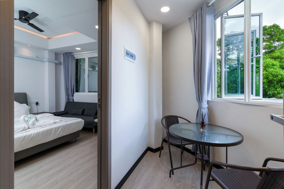 A hotel room with a bed, a small table with chairs, a window with curtains, and a ceiling fan.