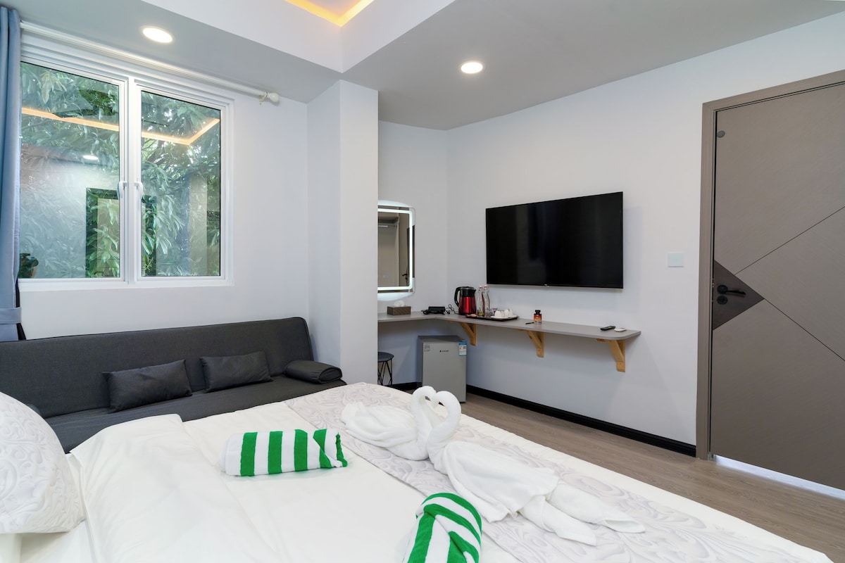 Une chambre d’hôtel moderne équipée d’un lit, d’un canapé, d’une télévision, d’une petite kitchenette et d’une porte.