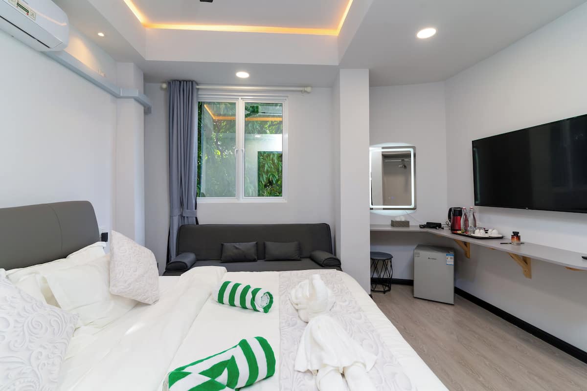 Une chambre d’hôtel moderne équipée d’un lit, d’un canapé, d’une petite kitchenette, d’une télévision et d’une fenêtre avec des rideaux.