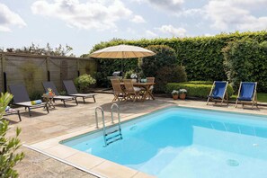 Una piscina con lettini, un tavolo e un ombrellone.