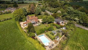 A large house with a swimming pool, surrounded by lush greenery and fields. - House & Annexe, Sleeps 18, Heated Pool (Sidlesham)