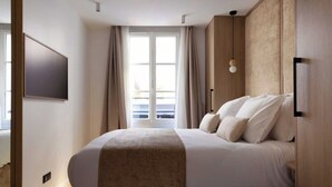 A modern bedroom with a large bed, a TV mounted on the wall, and a balcony visible through the window. - Superb air-conditioned apartment - Le Marais (Paris)