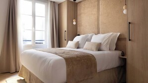 A modern bedroom with a large bed, wooden headboard, and a view of the city through a large window. - Superb air-conditioned apartment - Le Marais (Paris)