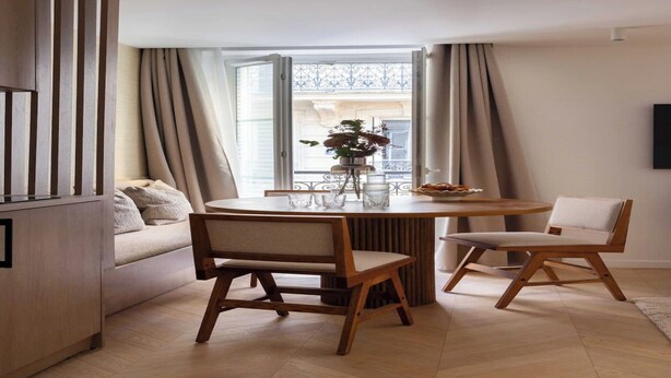 A modern living room with a round wooden table, two chairs, a sofa, and a large window with curtains. - Superb air-conditioned apartment - Le Marais (Paris)