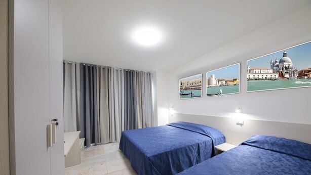 A hotel room with two beds, a view of a cityscape, and a window with curtains. - M9 REST HOUSE VENICE (Mestre)