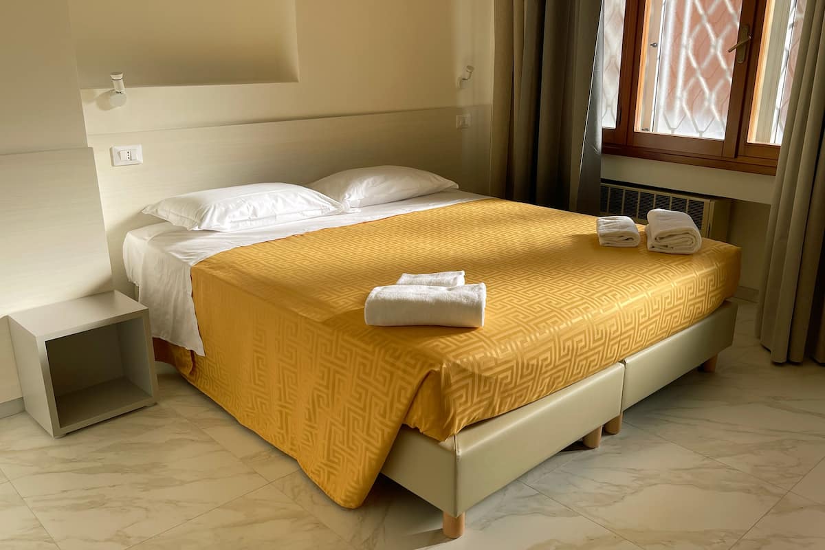 A neatly made bed with a patterned bedspread, two pillows, and two folded towels on the bed.