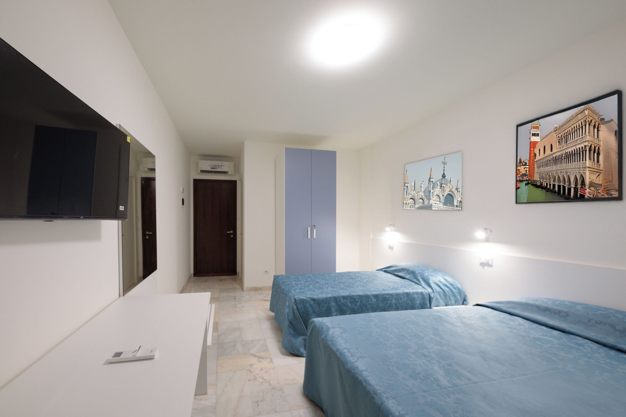 Ein Hotelzimmer mit zwei Einzelbetten, einem großen Kleiderschrank, einem Flachbildfernseher und einer Wand-Klimaanlage.