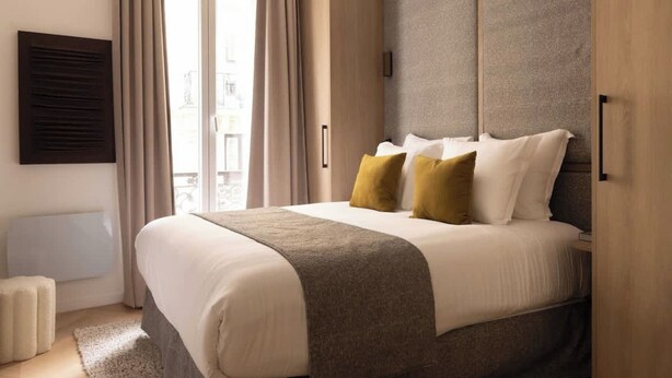 A modern hotel room with a large bed, a built-in wardrobe, and a view of the city through the window. - Elegant apartment with AC - Le Marais (Paris)