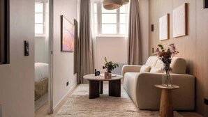 A modern living room with a sofa, a coffee table, and a vase with flowers. There are curtains, a window, and wall art. - Elegant apartment - AC- 2BR-6P- le Marais (Paris)