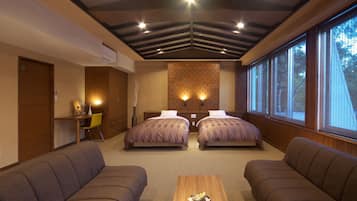 A hotel room with two beds, a desk, a chair, and large windows.