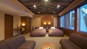 Quarto de hotel com duas camas, uma escrivaninha, uma cadeira e janelas amplas.