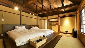 Une pièce de style japonais traditionnel, avec un sol recouvert de tatamis, un plafond bas en bois et un lit avec du linge de lit blanc.