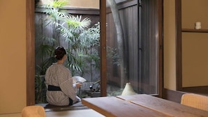Une pièce de style japonais traditionnel, avec un sol recouvert de tatamis, une porte coulissante donnant sur un jardin et une petite table en bois.