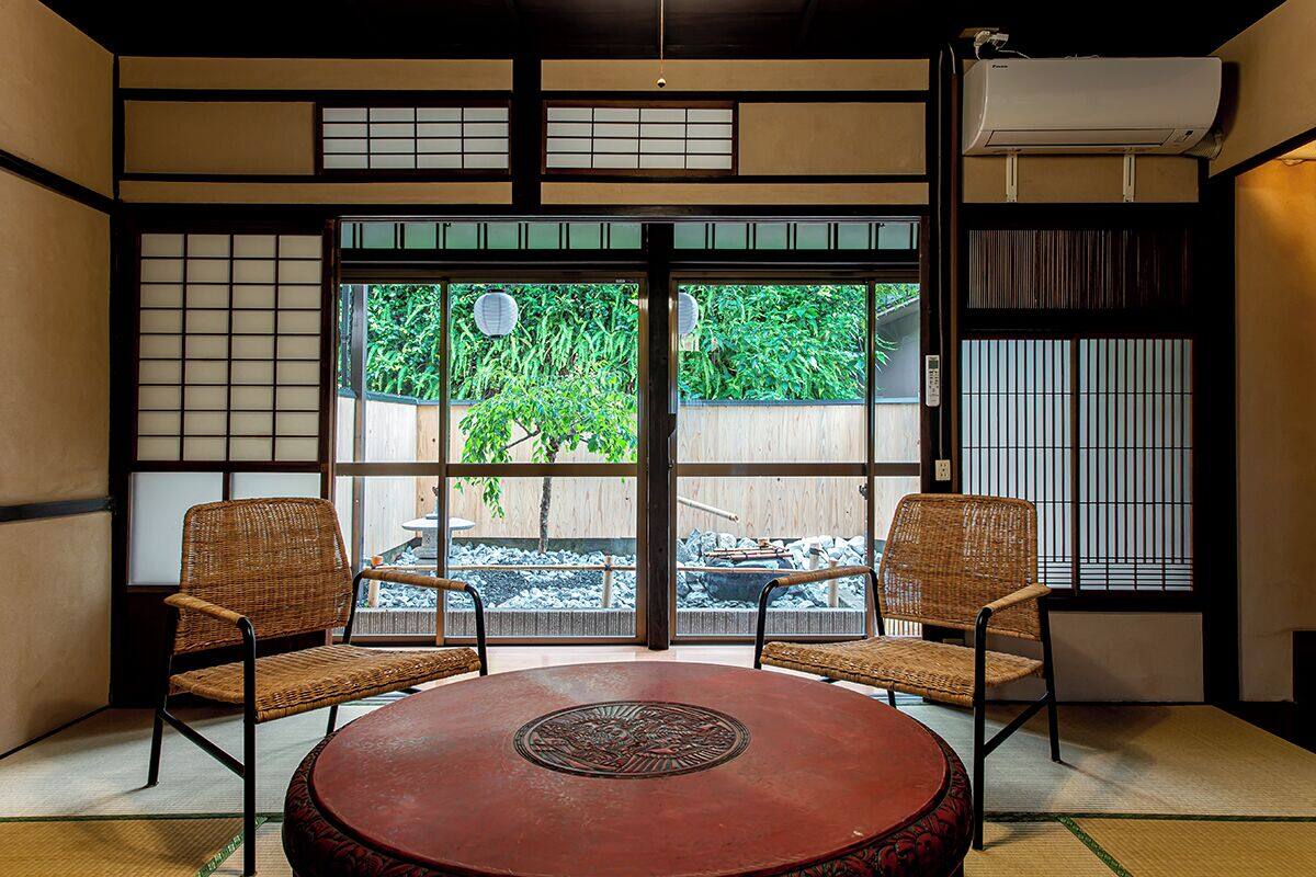 A traditional Japanese room with tatami flooring, a low table with a decorative centerpiece, and sliding doors leading to an outdoor garden.