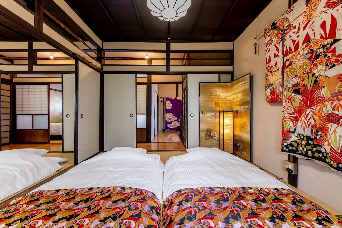A traditional Japanese-style room with tatami flooring, a low wooden ceiling, and sliding doors leading to another room.