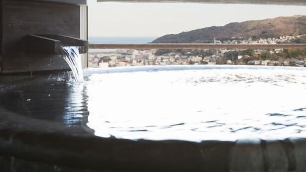 A view from a window overlooking a body of water with a distant town and hills. - Bettei Sora no ue (Ito)