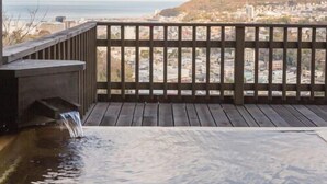 A wooden deck with a water feature and a view of a cityscape and hills in the distance. - Bettei Sora no ue (Ito)
