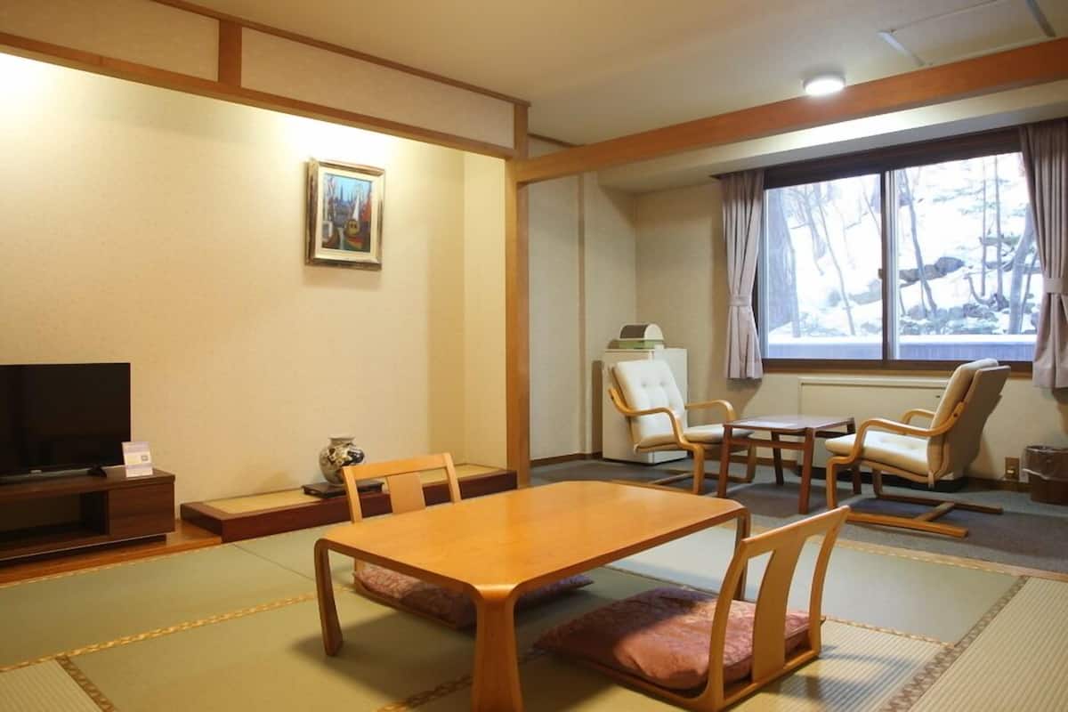 A traditional Japanese-style room with tatami flooring, a low table, chairs, a television, and a window with curtains.