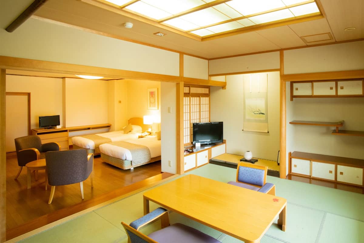 A traditional Japanese-style room with tatami flooring, a television, a desk, and a bed.