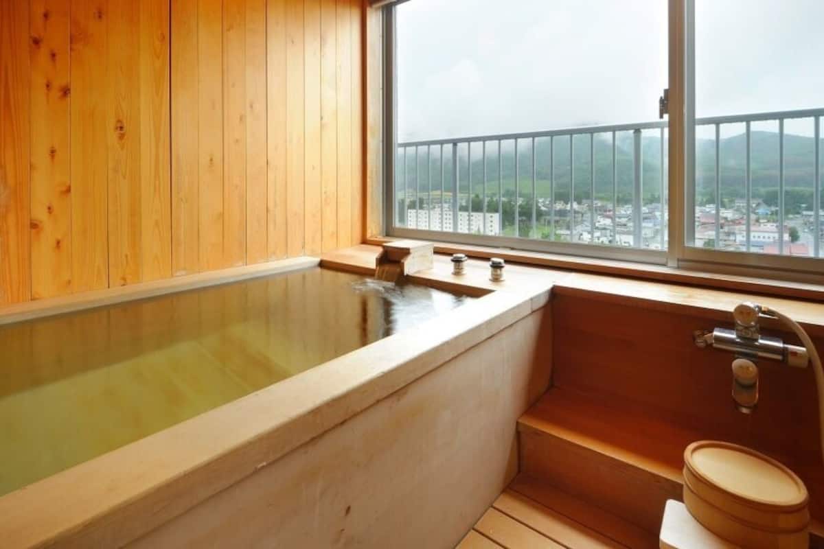 A wooden room with a large bathtub, a window with a view, and a wooden toilet.