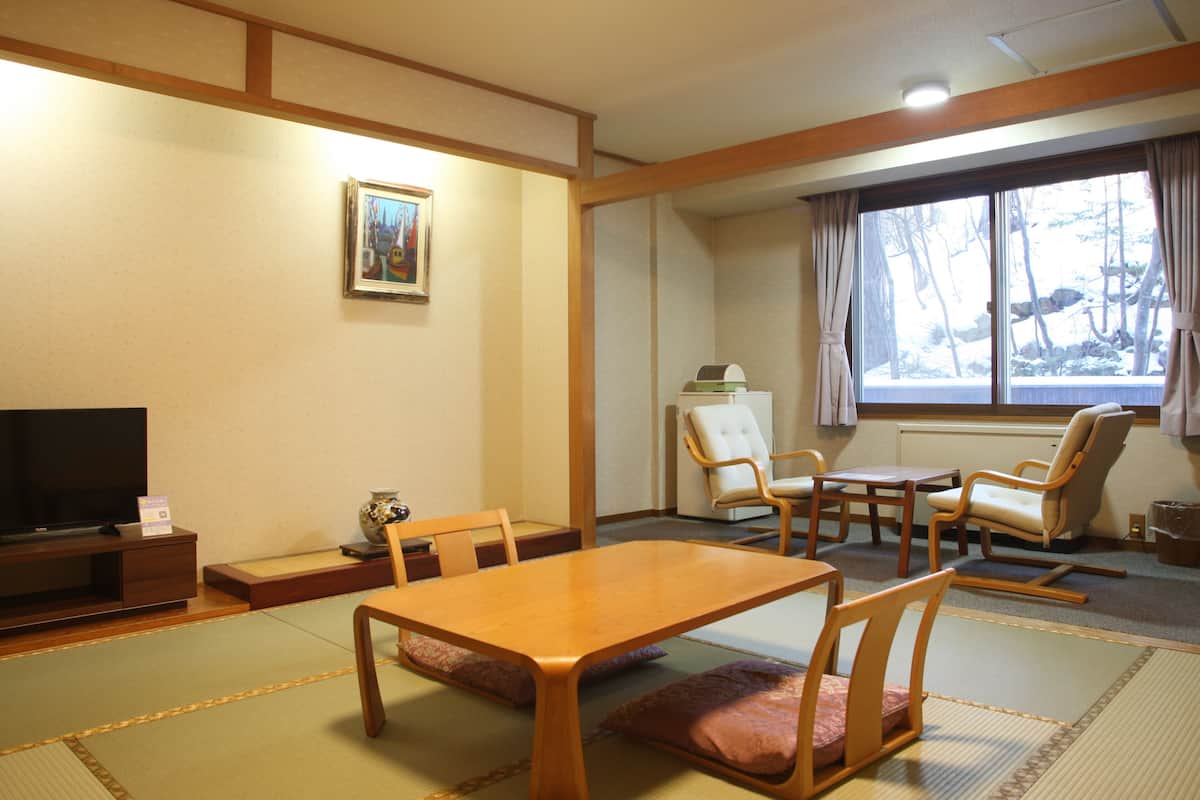 A traditional Japanese-style room with tatami flooring, a television, a painting, and a view of a snowy landscape through the window.
