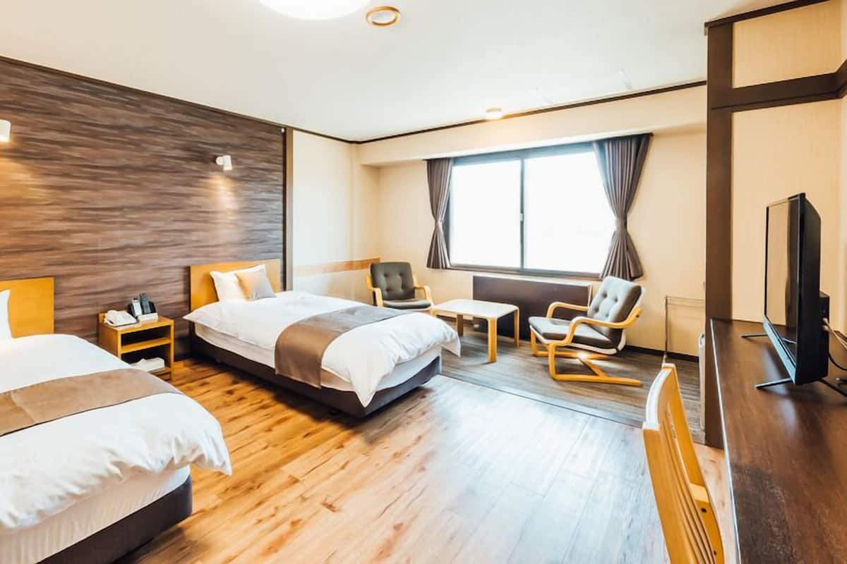 A hotel room with two beds, a desk, a chair, a TV, and a window with curtains.
