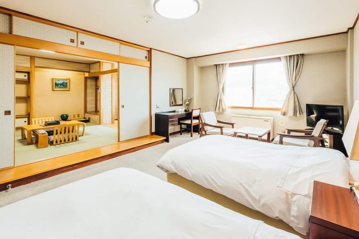 A hotel room with two beds, a desk, a chair, a TV, and a large mirror.