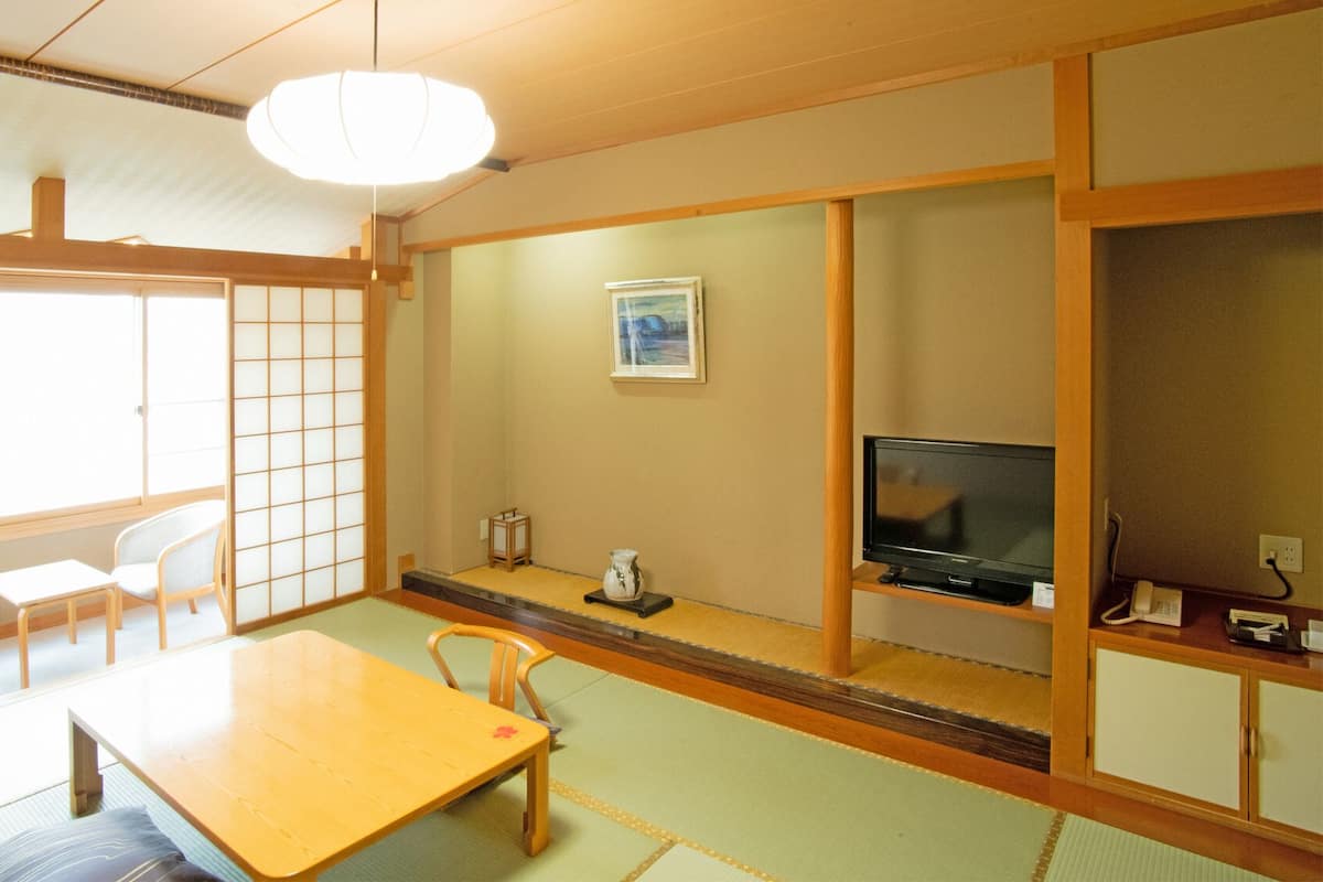 A traditional Japanese room with tatami flooring, a low table, chairs, a television, and a shoji screen.